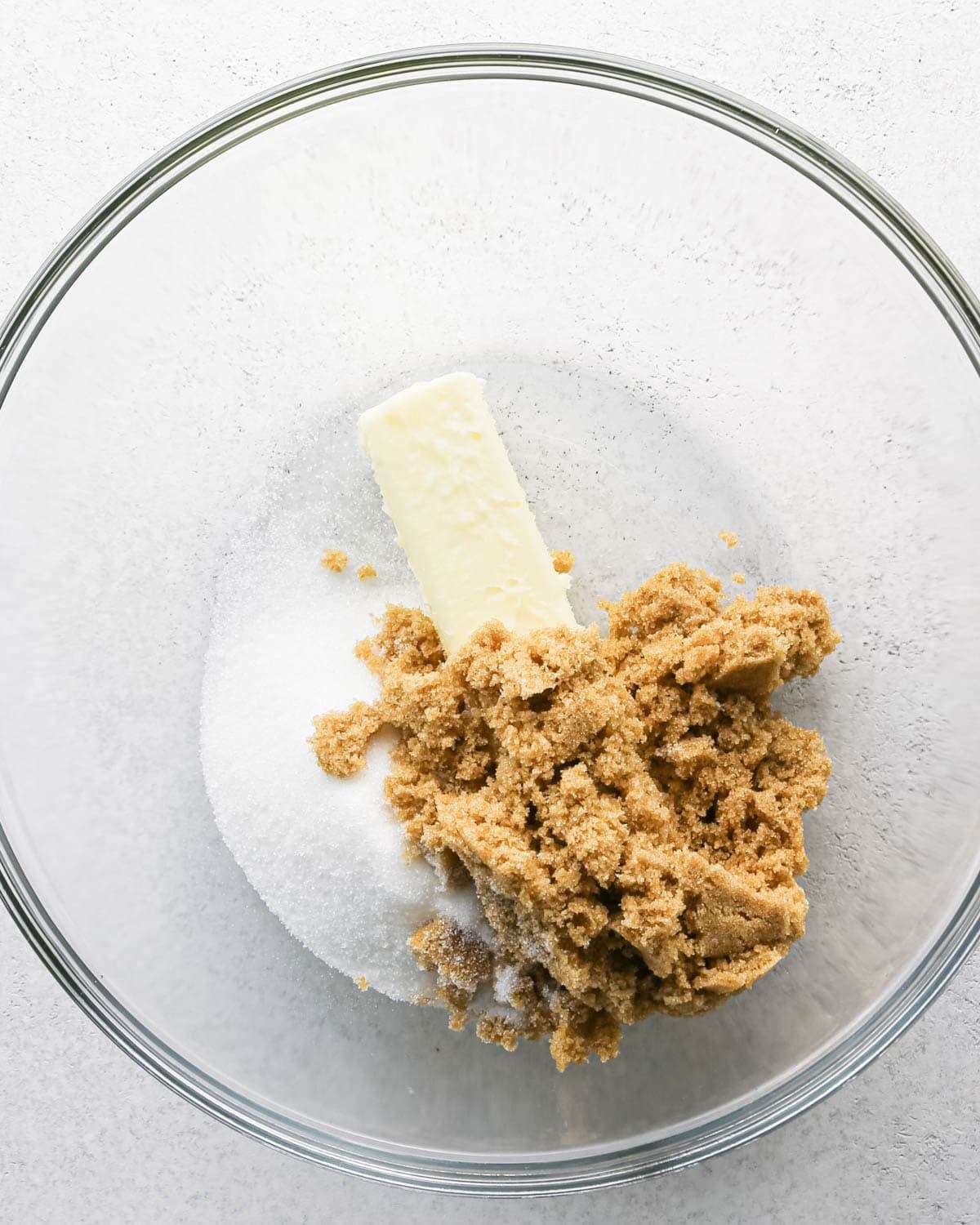 Making chocolate chip cashew cookies: overhead photo of butter, sugar, and brown sugar in a large clear mixing bowl.