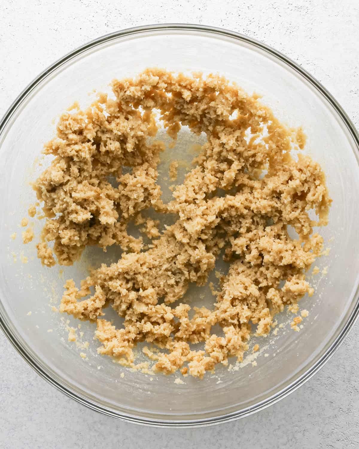 Making chocolate chip cashew cookies: overhead photo of butter, sugar, and brown sugar creamed together in a large clear mixing bowl.