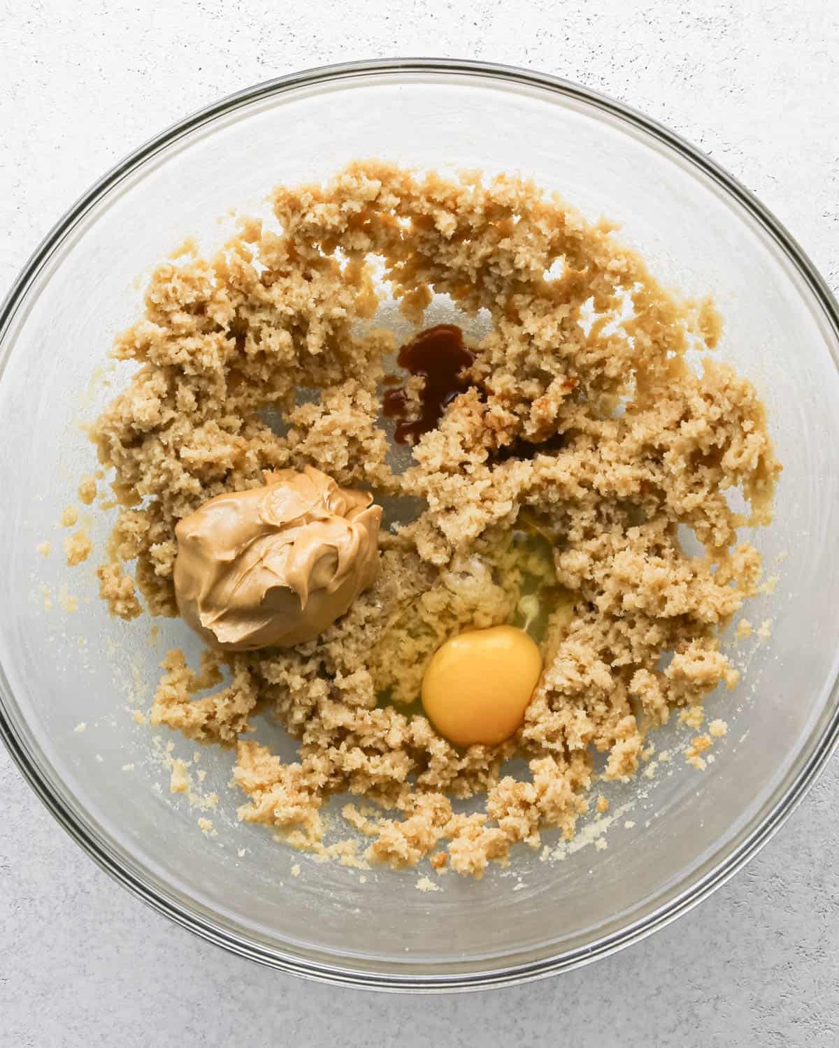 Making chocolate chip cashew cookies: overhead photo of egg, vanilla, and cashew butter added to the butter and sugar mixture in a large clear mixing bowl.