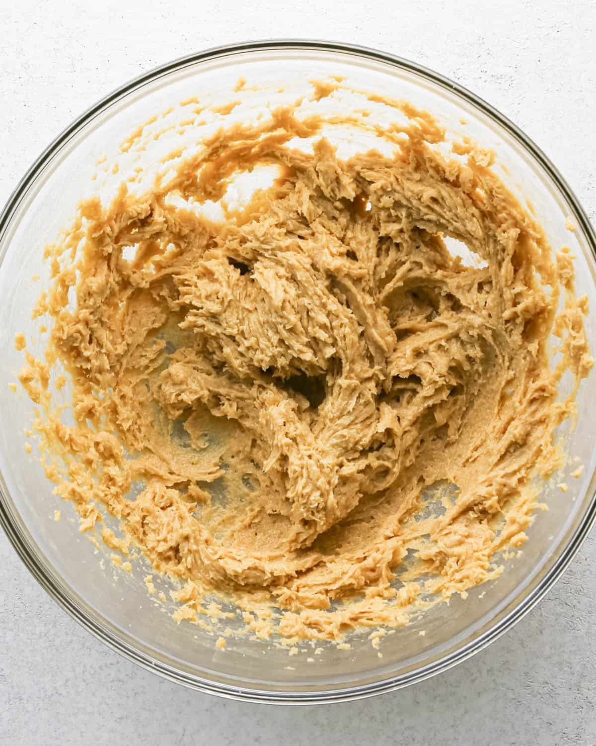 Making chocolate chip cashew cookies: overhead photo of egg, vanilla, cashew butter, butter, and sugar mixed together in a large clear mixing bowl.