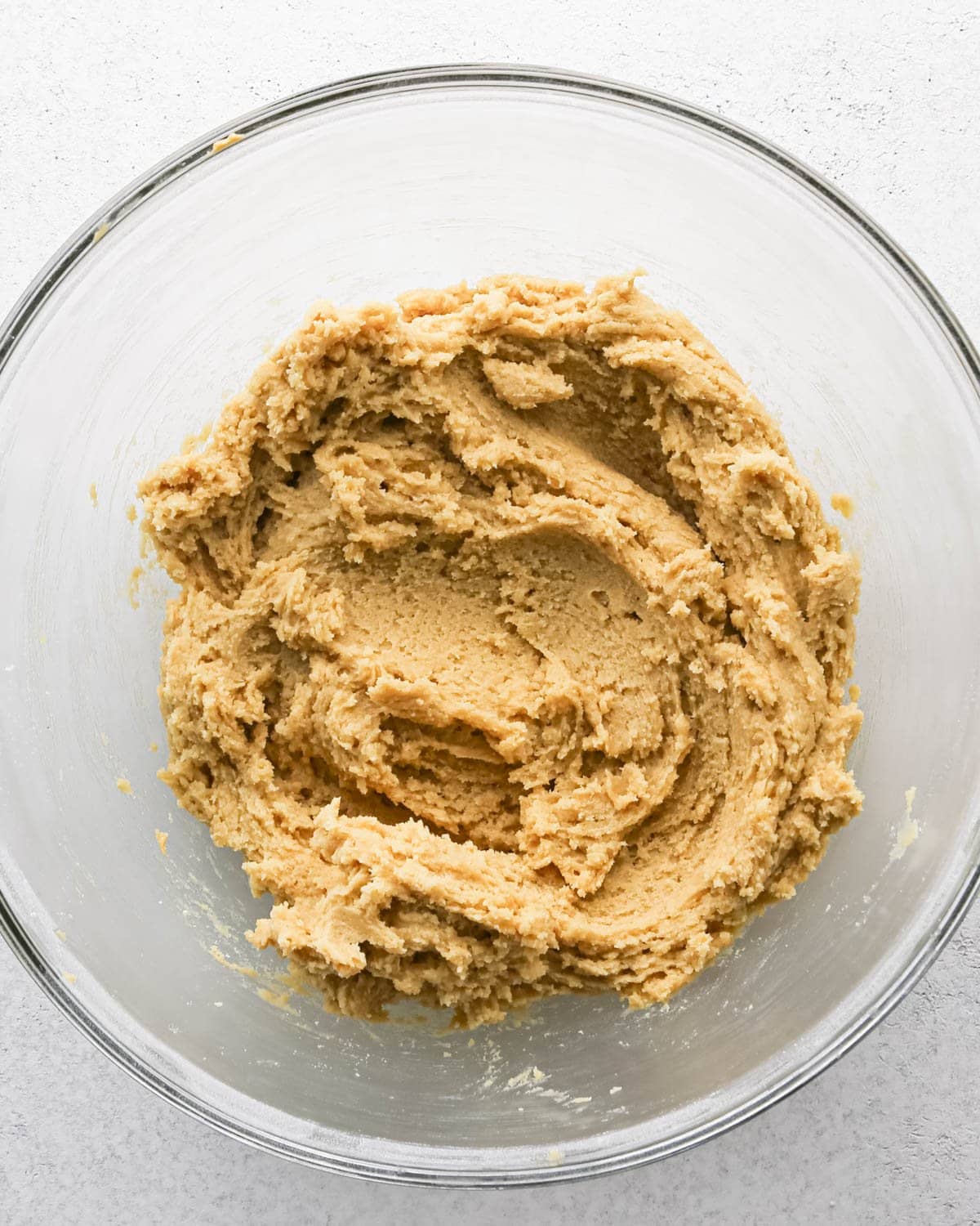 Making chocolate chip cashew cookies: overhead photo of wet and dry ingredients for cashew cookies mixed together in a large clear mixing bowl.