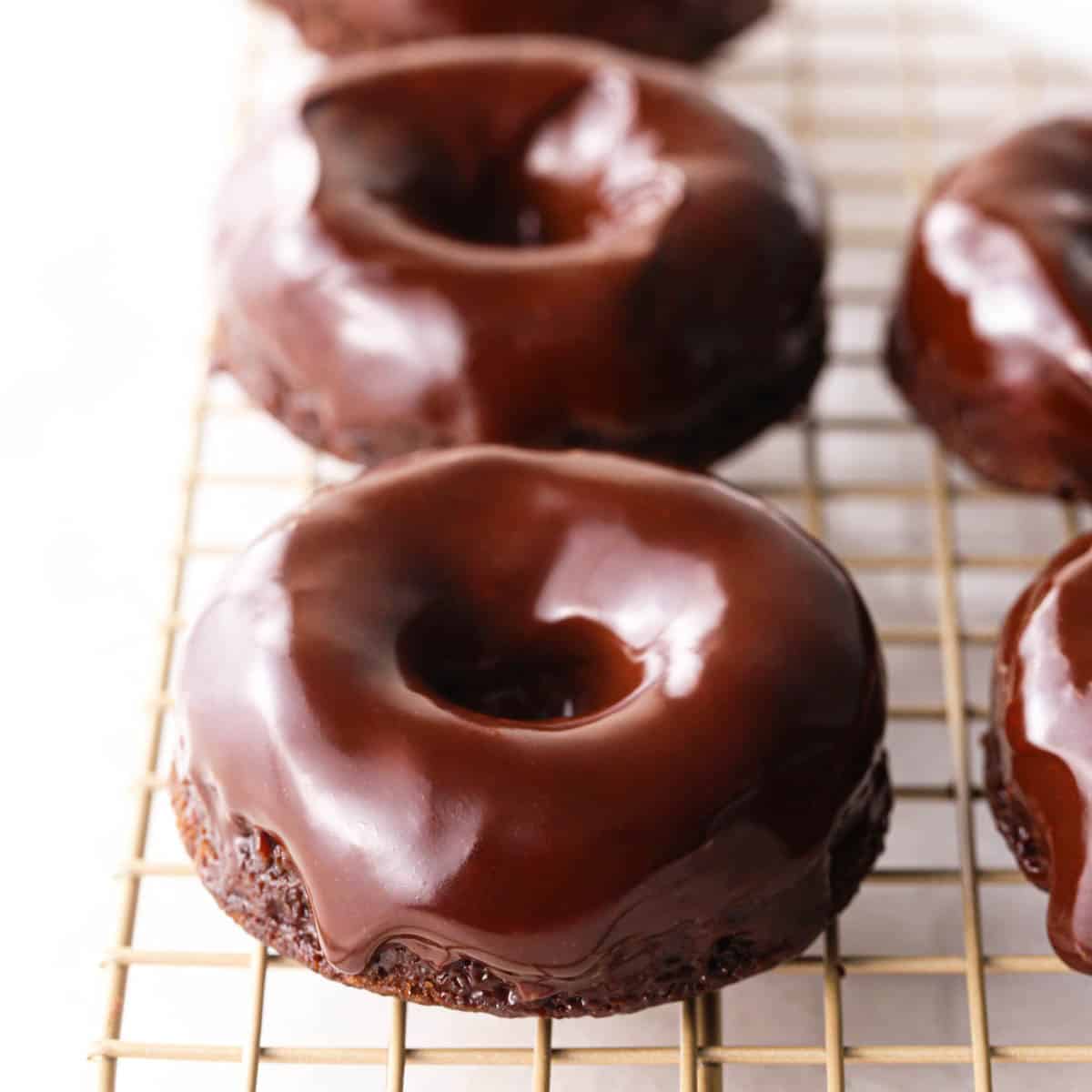 5 donuts covered in chocolate glaze on a gold wire cooling rack