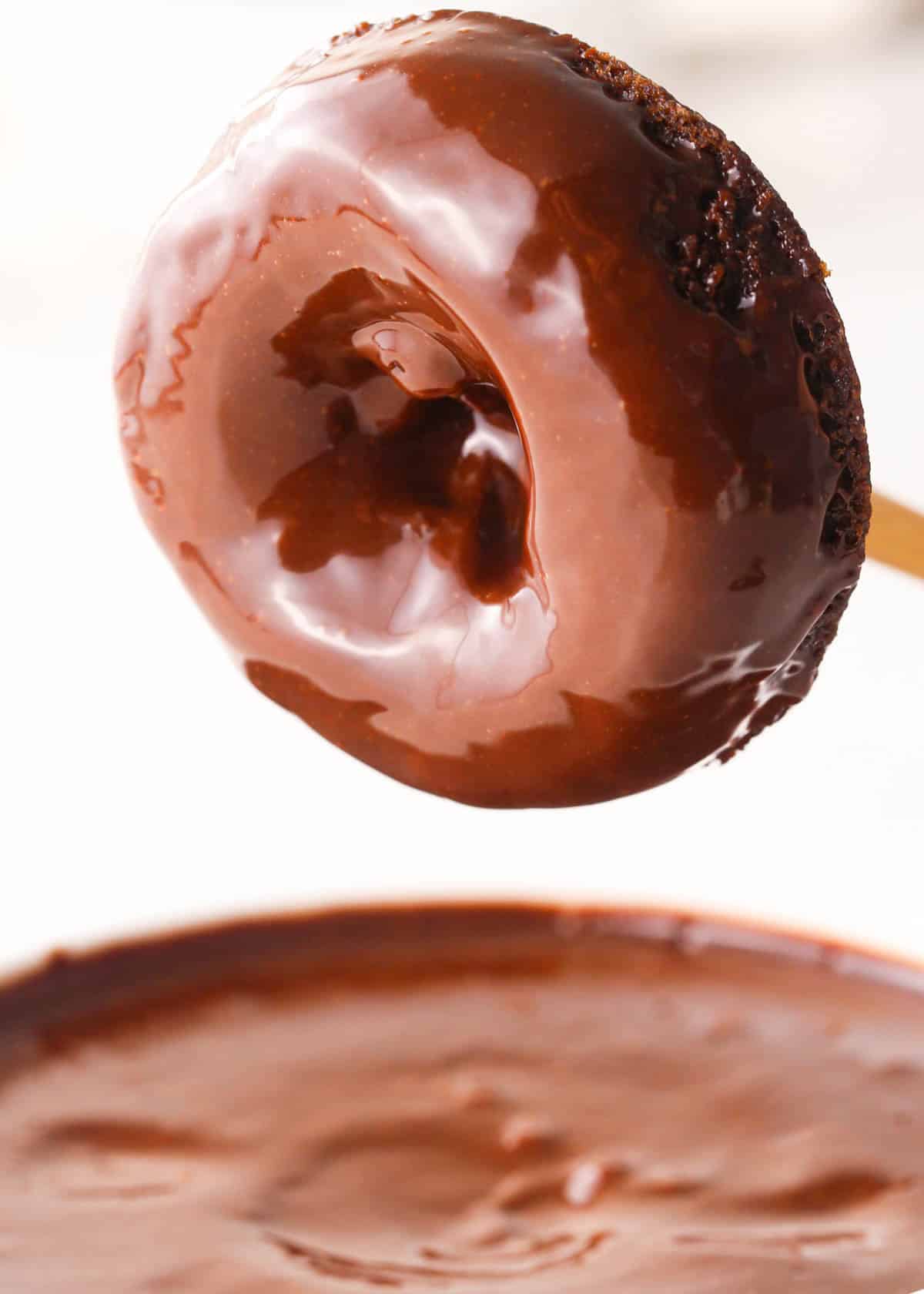 a donut just after bing dipped in chocolate glaze hovering over a bowl of chocolate glaze
