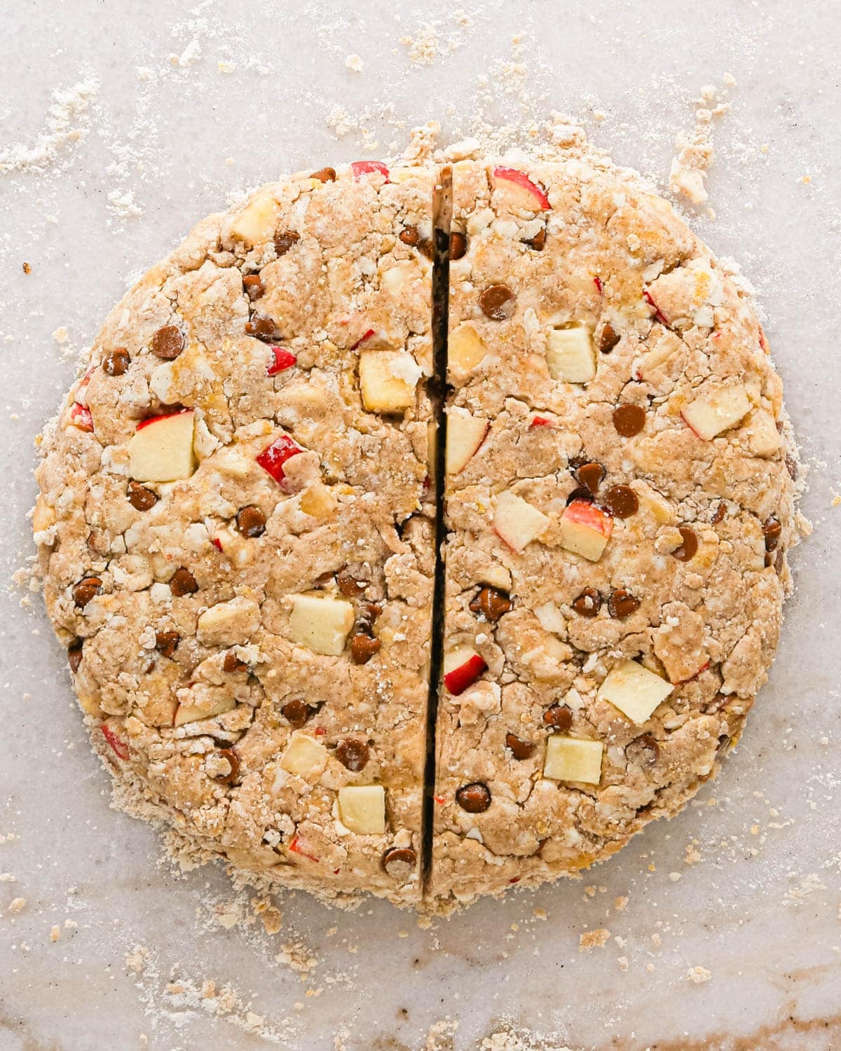apple scones dough formed into a round disc, cut in half from top to bottom on a marble surface