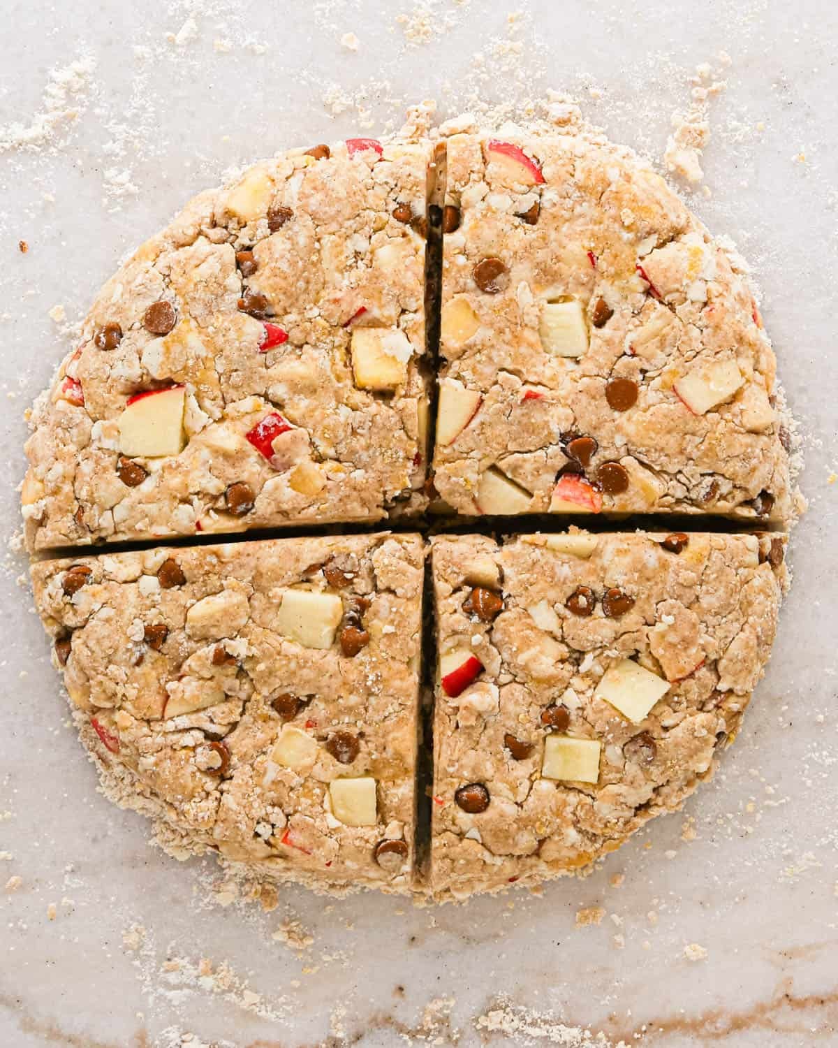 apple scones dough formed into a round disc, cut in half fourths on a marble surface