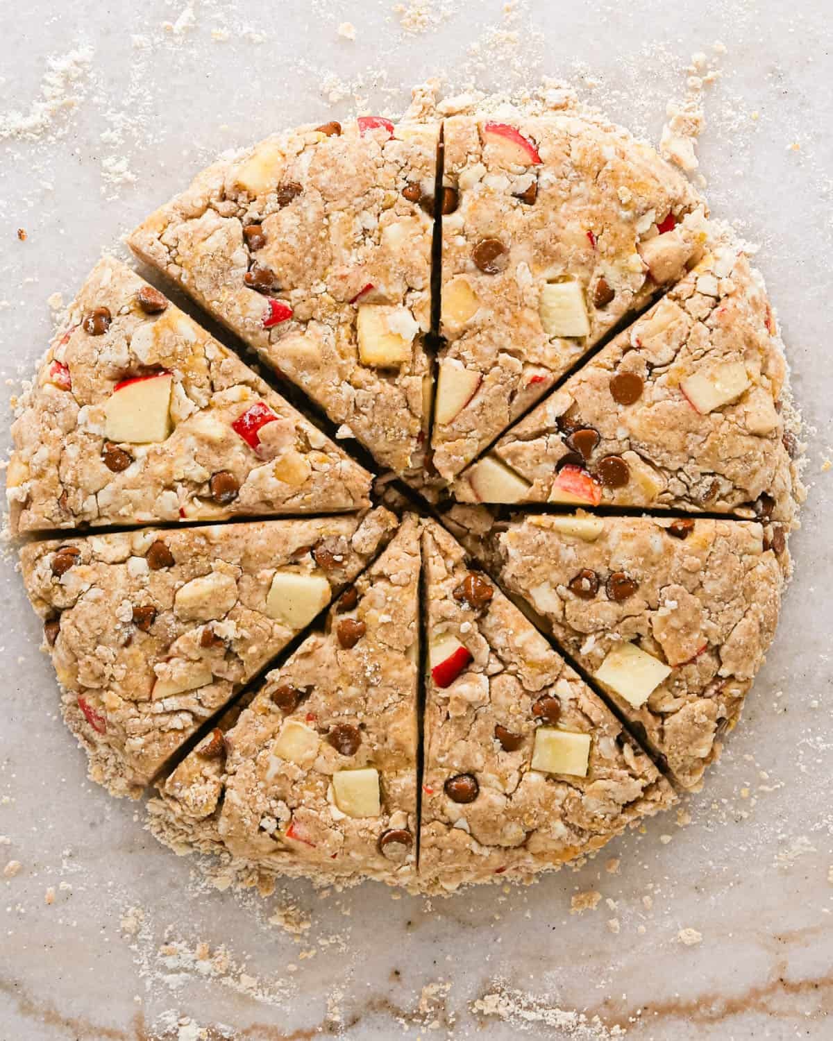 apple scones dough formed into a round disc, cut in half eighths on a marble surface