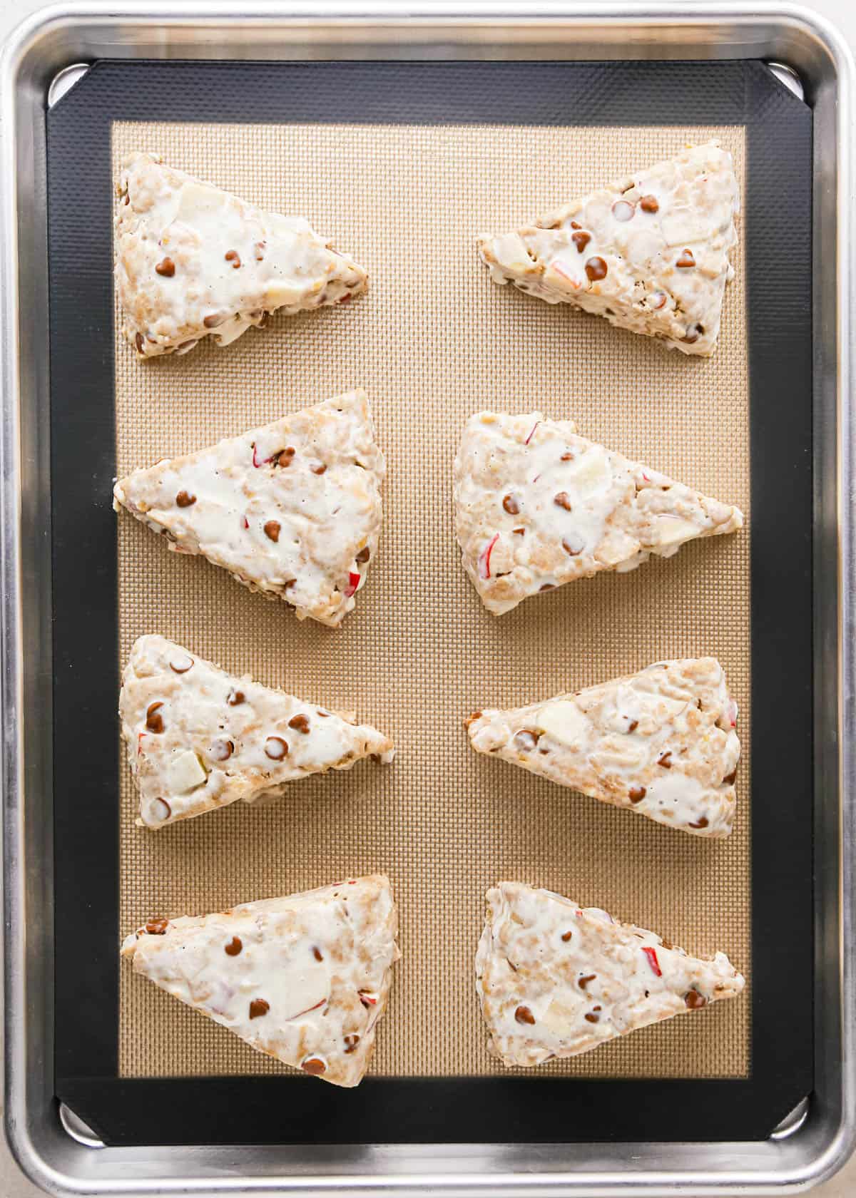 8 apple scones on a baking sheet lined with a silicone baking mat brushed with heavy cream