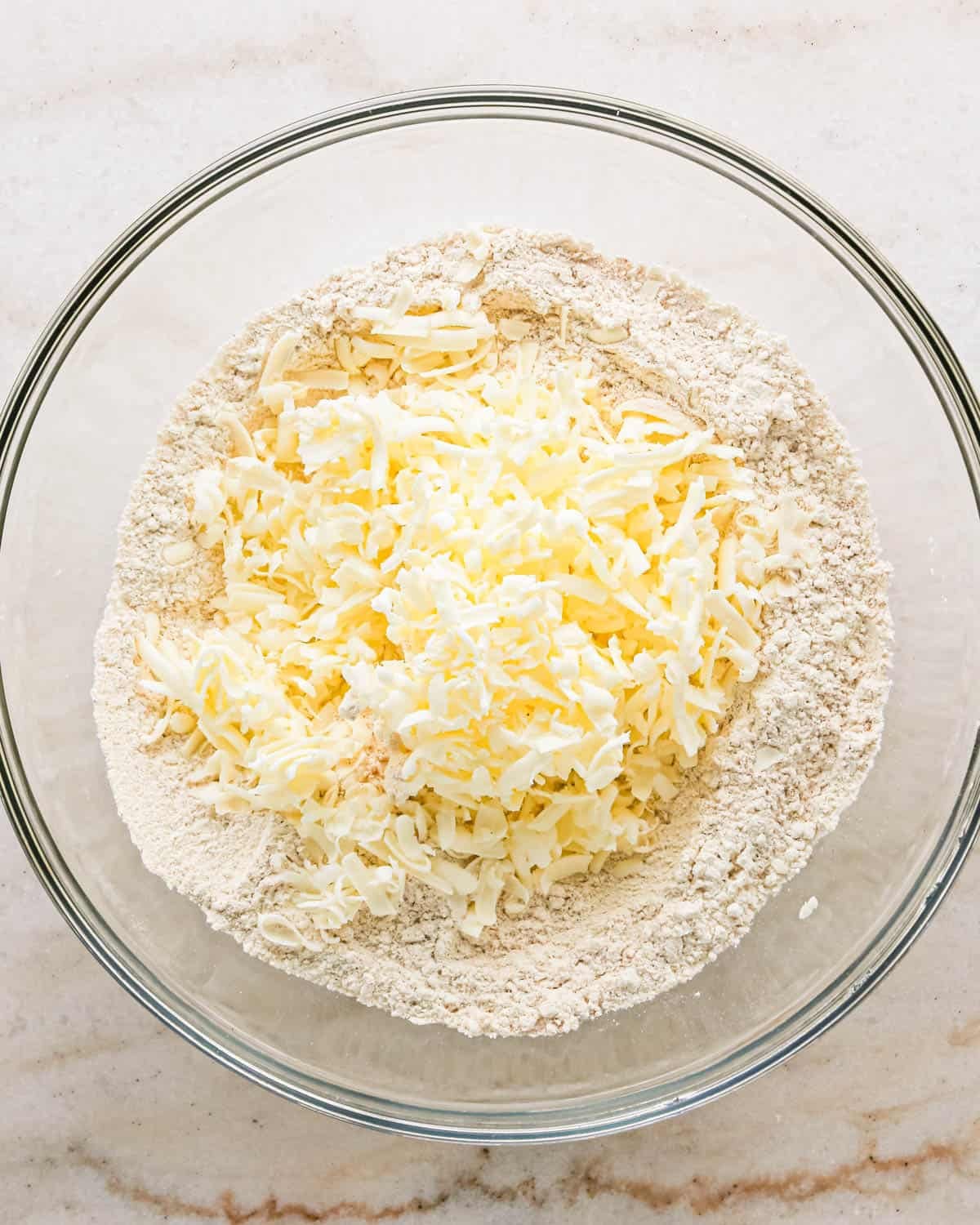 making apple scones - grated butter added to the dry ingredient mixture in a glass bowl before mixing