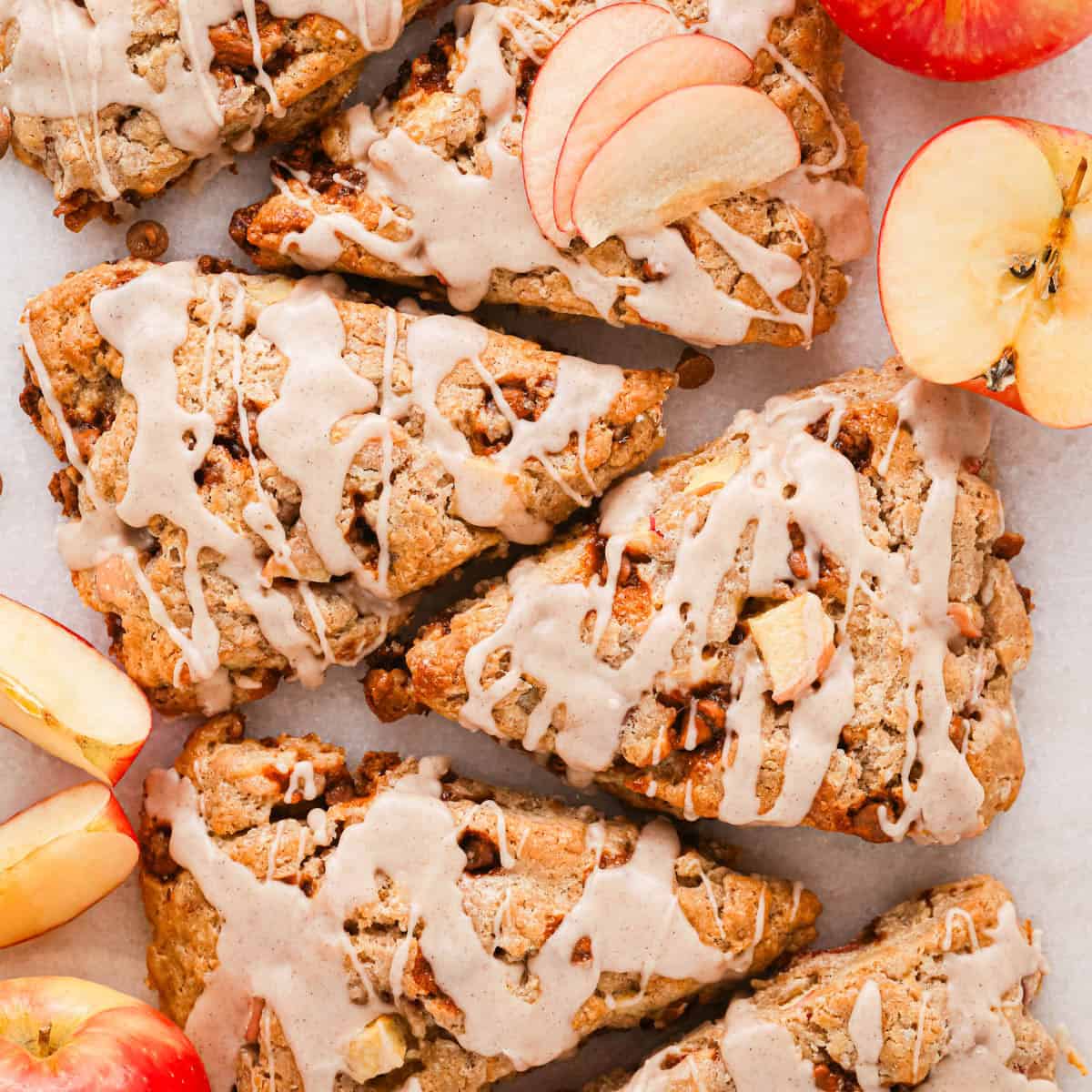 overhead photo of 6 cinnamon apple scones on a marble serving plate topped with cinnamon glaze, the middle one has 3 apple slices on it and they are surrounded by cinnamon chips and sliced apples