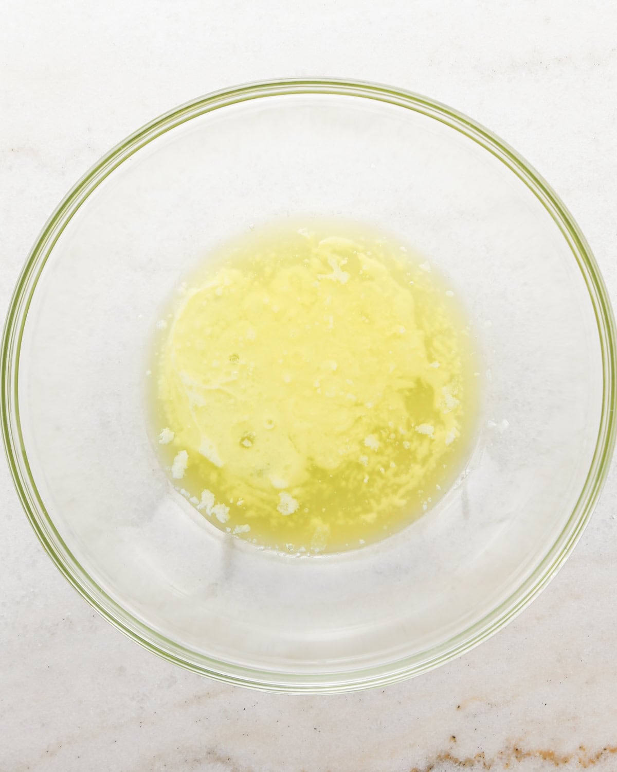 Making coconut cupcakes: overhead photo of wet ingredients for coconut cupcakes added to a clear mixing bowl.