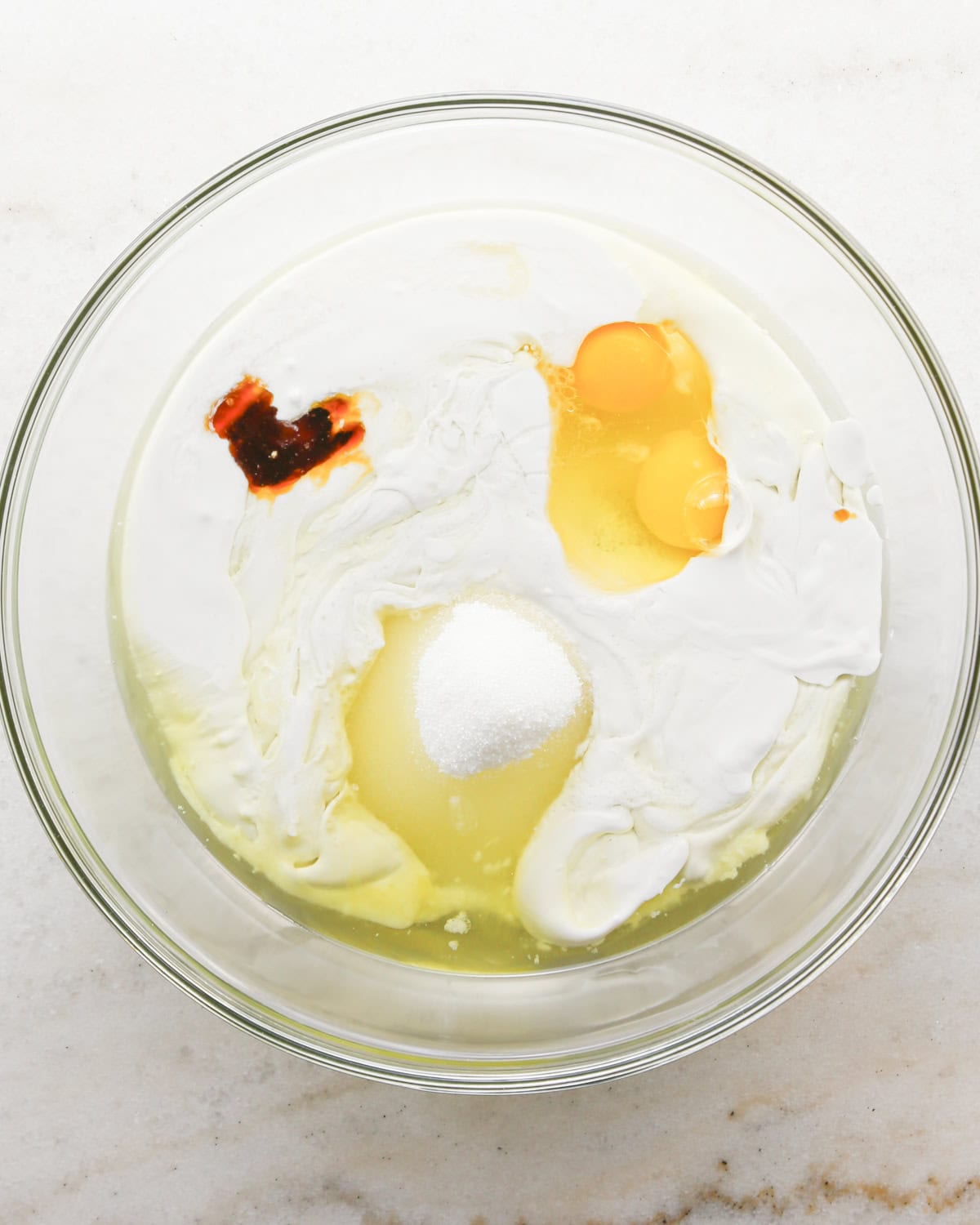 Making coconut cupcakes: overhead photo of wet ingredients for coconut cupcakes added to a clear mixing bowl.