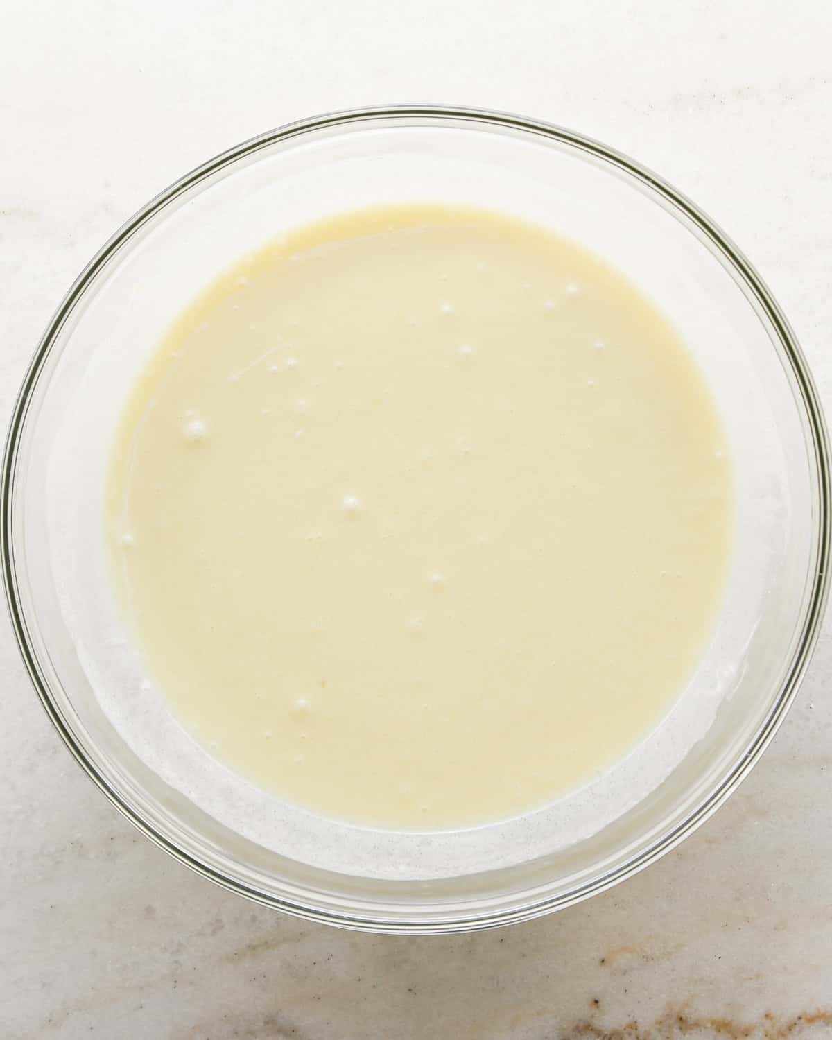 Making coconut cupcakes: overhead photo of wet ingredients for coconut cupcakes added to a clear mixing bowl and mixed together.