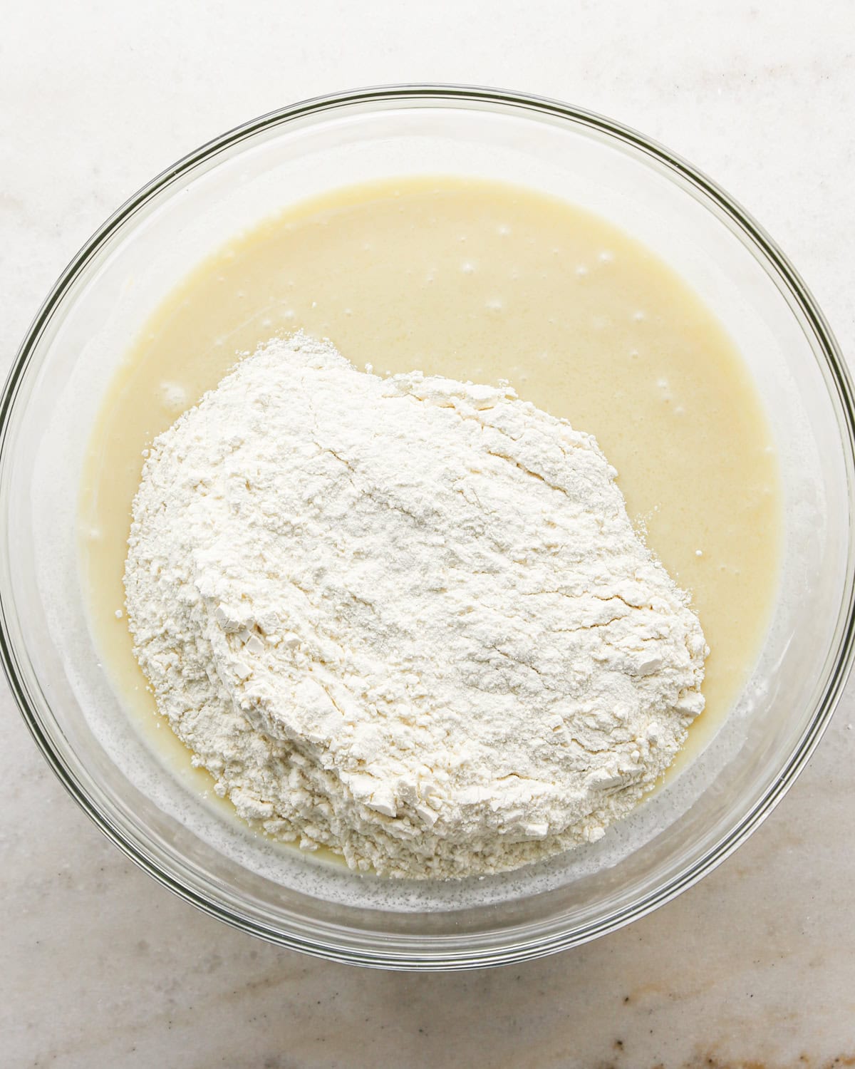 Making coconut cupcakes: overhead photo of wet and dry ingredients for coconut cupcakes being combined in a clear mixing bowl.