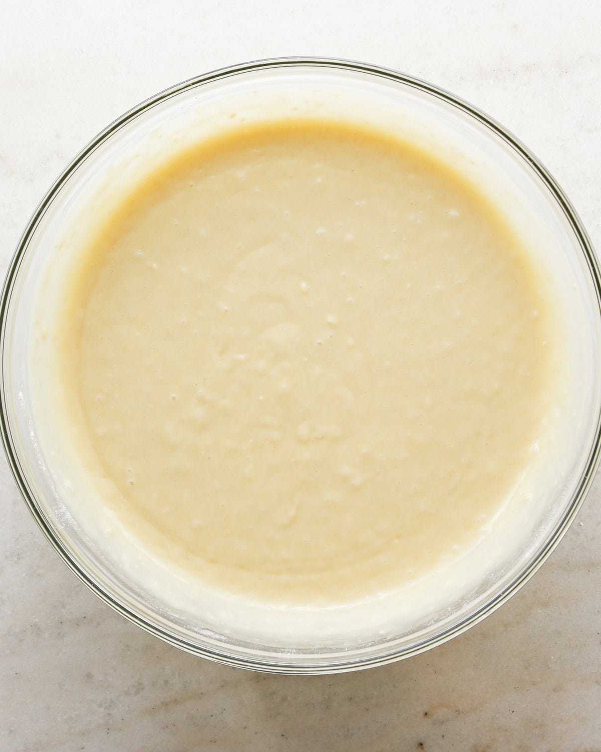 Making coconut cupcakes: overhead photo of wet and dry ingredients for coconut cupcakes combined in a clear mixing bowl and mixed together.