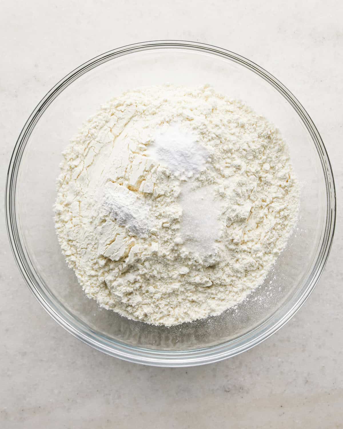 Making coconut cupcakes: overhead photo of dry ingredients for coconut cupcakes being added to a clear mixing bowl.