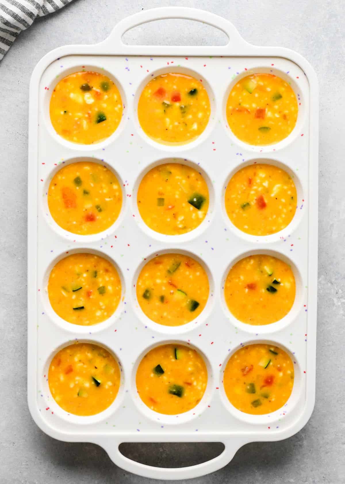 vegetable cottage cheese egg bites mixture in a white silicone muffin pan before baking