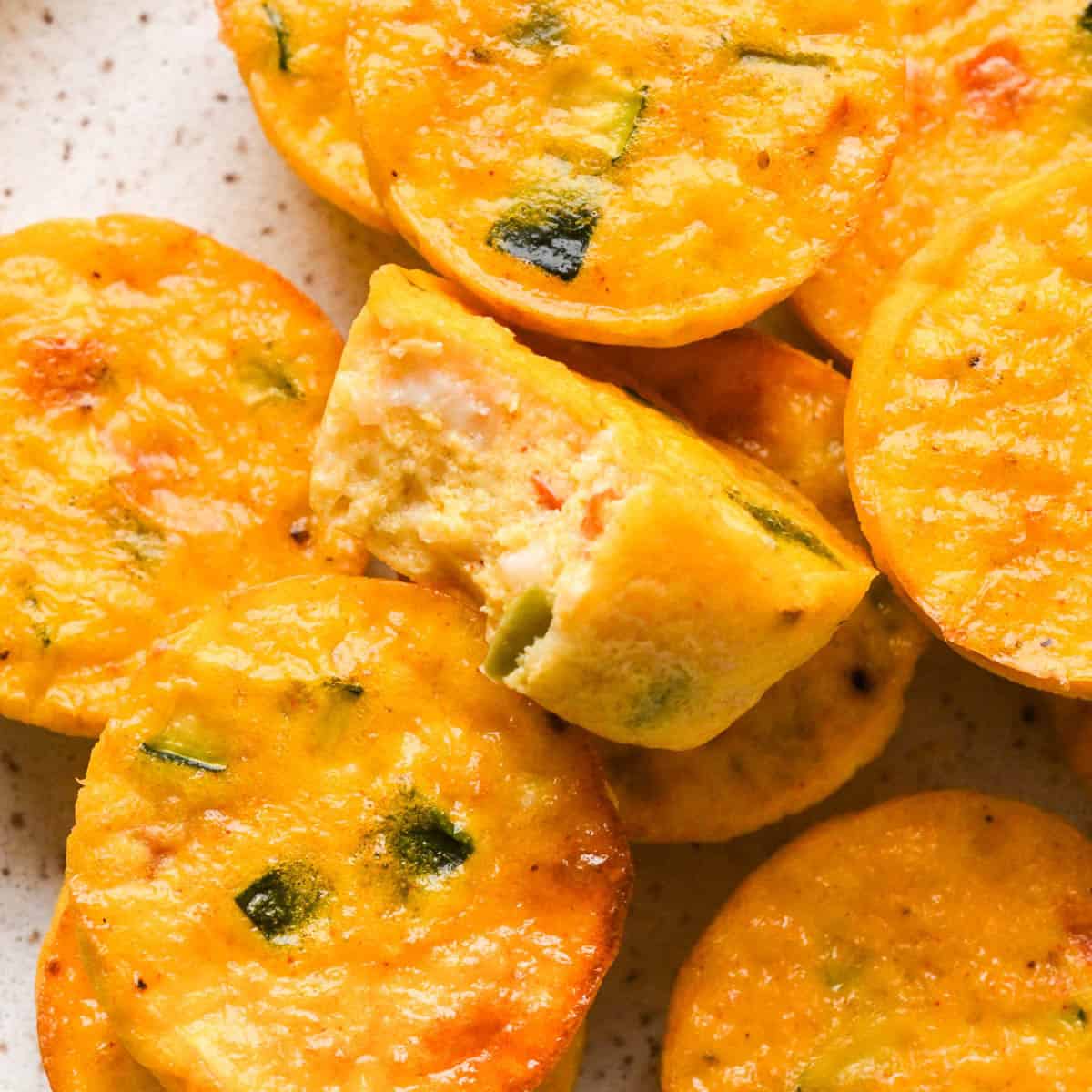 a pile of cottage cheese egg bites, the middle one has a bite taken out of it so the fully texture and vegetables on the inside are visible