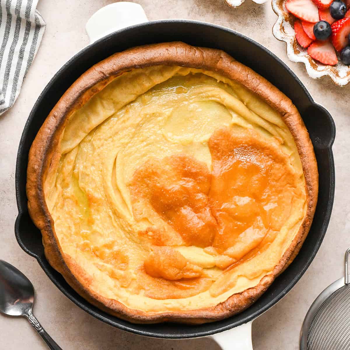 Overhead view of a golden, puffed Dutch baby pancake baked in a cast-iron skillet on a light countertop.