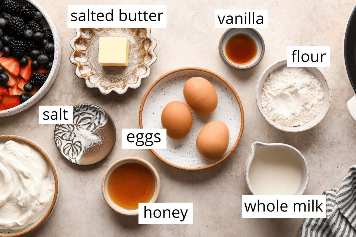 Overhead photo of the ingredients for a Dutch baby pancake, including eggs, honey, whole milk, flour, vanilla, salted butter, and salt.