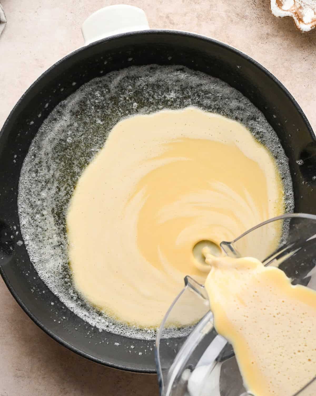 Making a Dutch baby: overhead view of Dutch baby pancake batter being added to the cast-iron skillet with the melted butter.