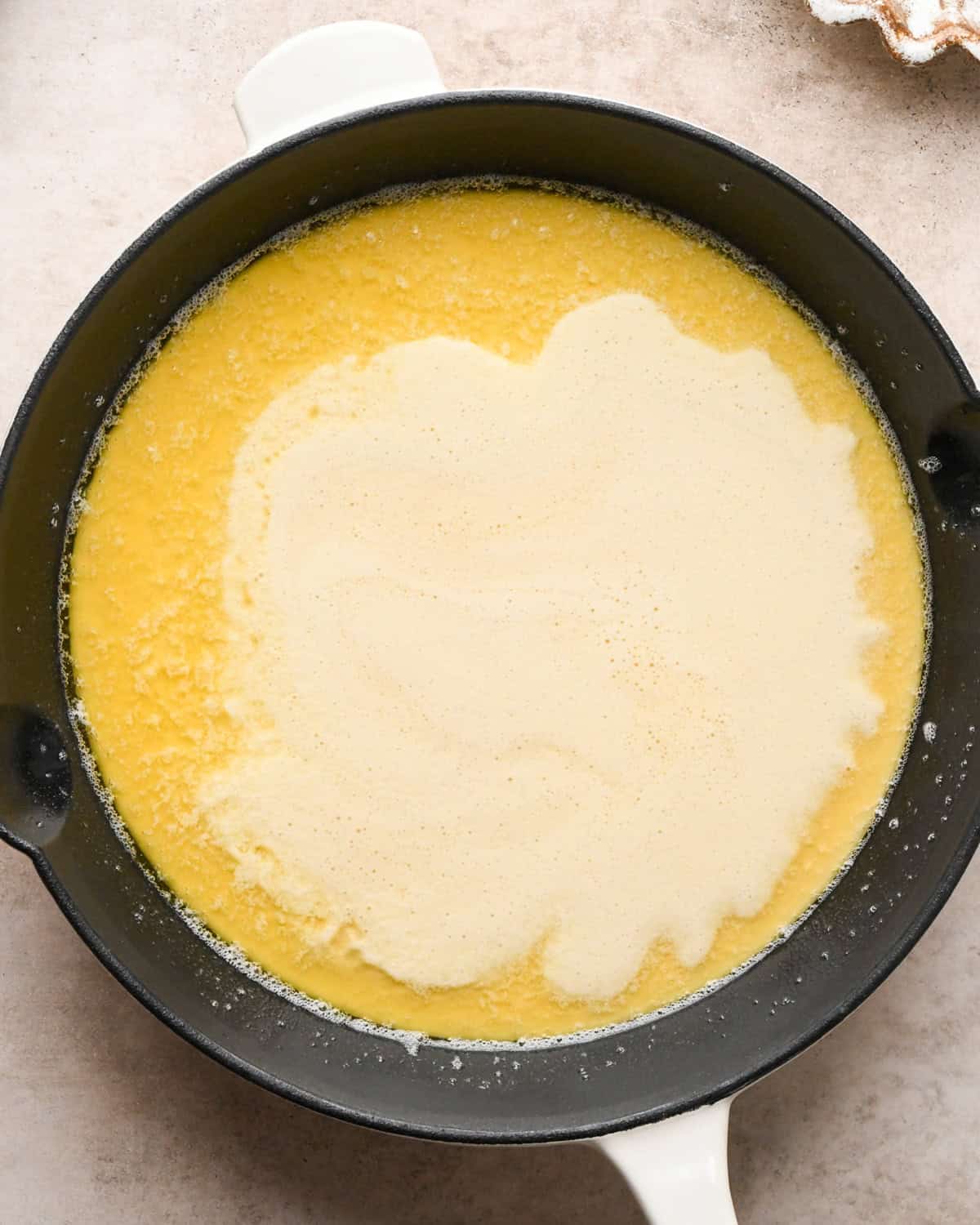 Making a Dutch baby: overhead view of Dutch baby pancake batter being added to the cast-iron skillet with the melted butter and spread over the surface of the skillet.