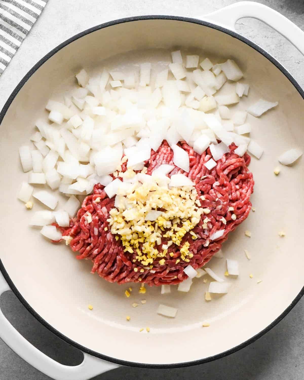 making ground beef stir fry - ground beef, garlic and onion in a white skillet before cooking