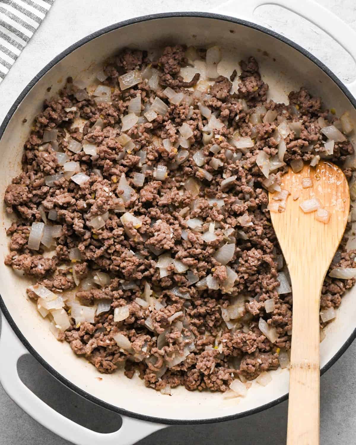 making ground beef stir fry - ground beef, garlic and onion in a white skillet after cooking