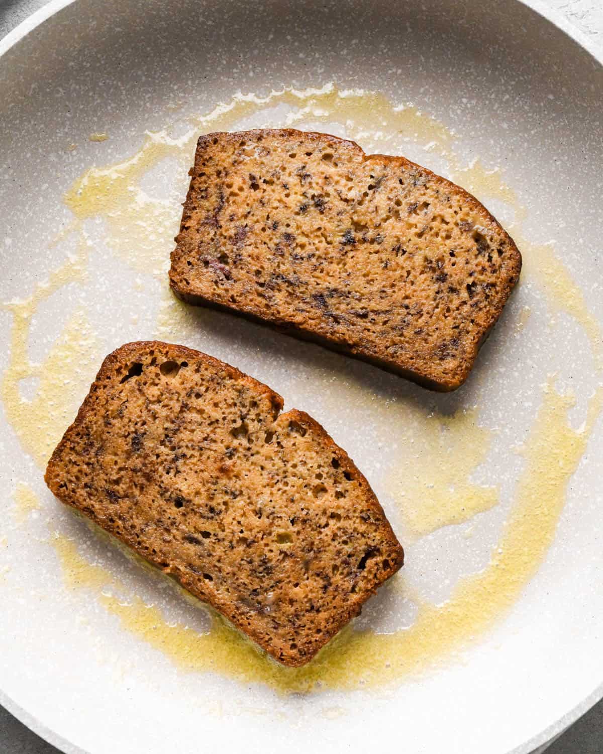 Making banana bread French toast: two pieces of banana bread after being dipped in the custard, cooking on the first side on a buttered skillet