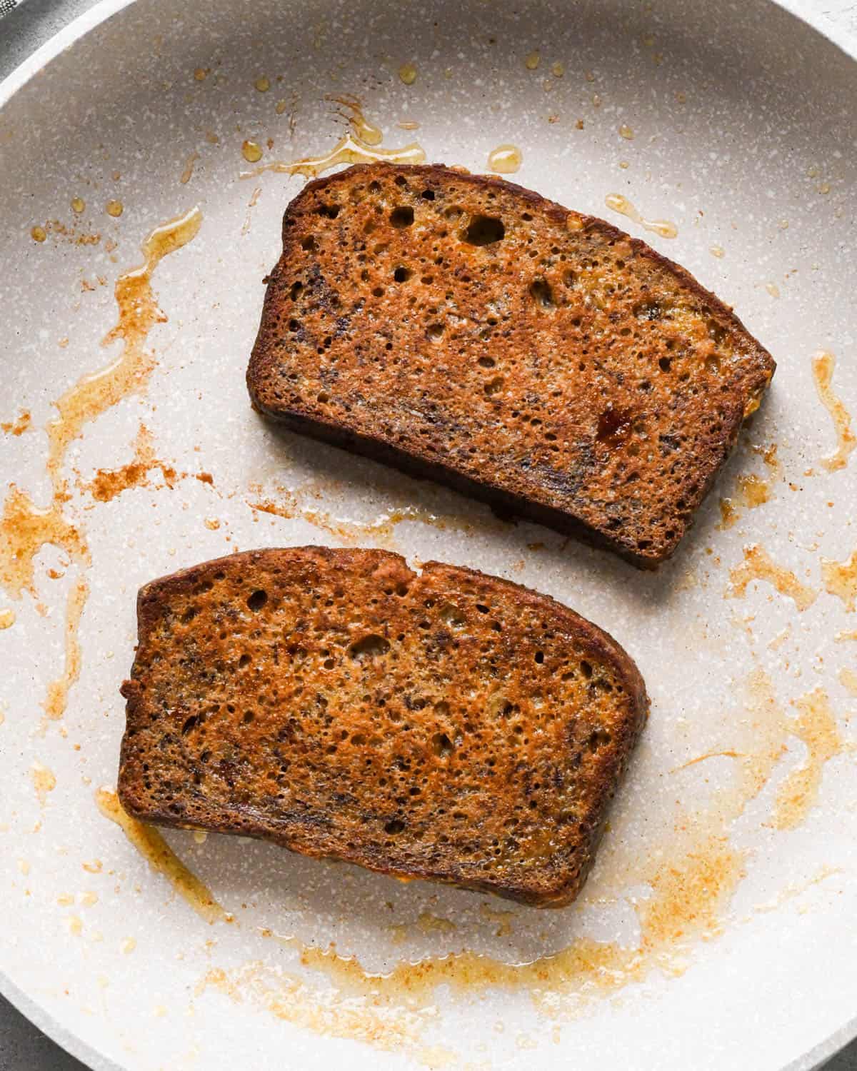 Making banana bread French toast: two pieces of banana bread cooking in a skillet