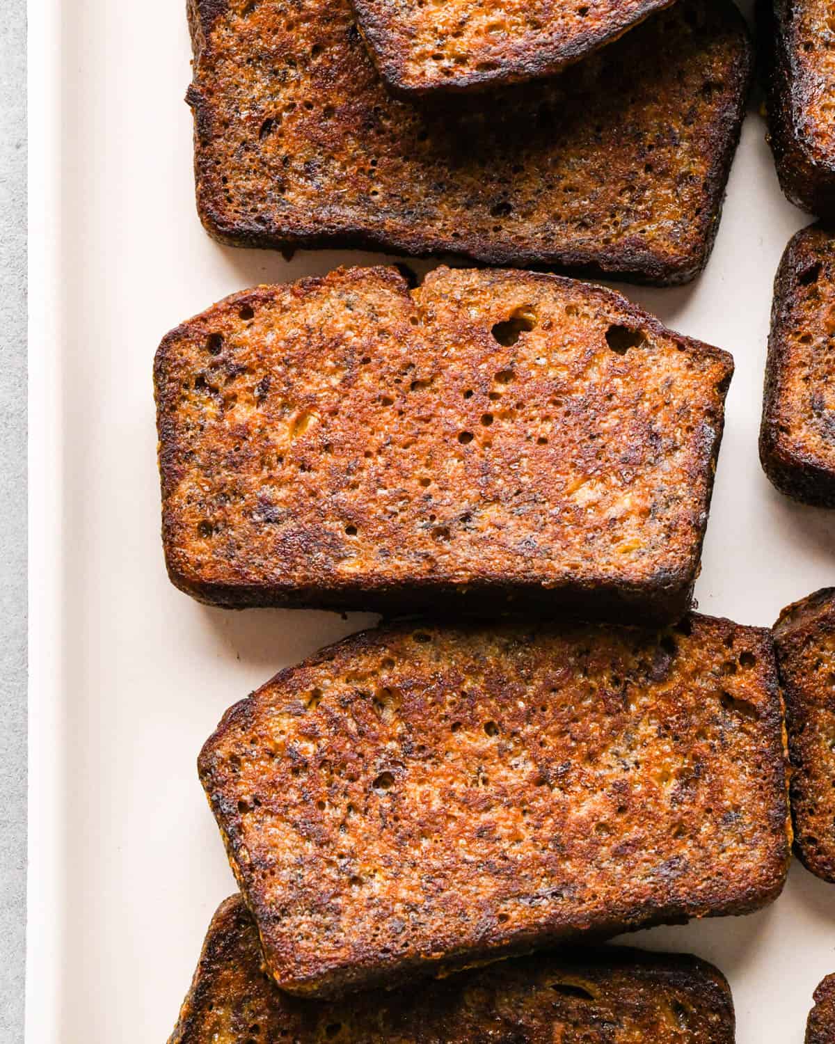 Making banana bread French toast: close-up photo of a white plate full of slices of banana bread French toast hot off the skillet.
