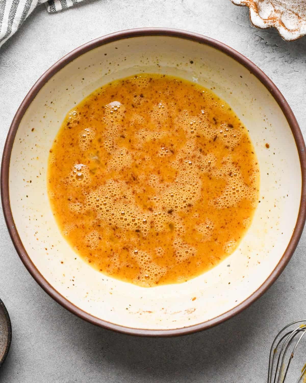 Making banana bread French toast: overhead photo of eggs, cinnamon, brown sugar, and vanilla sitting together in a white speckled bowl on a gray countertop and whisked together.