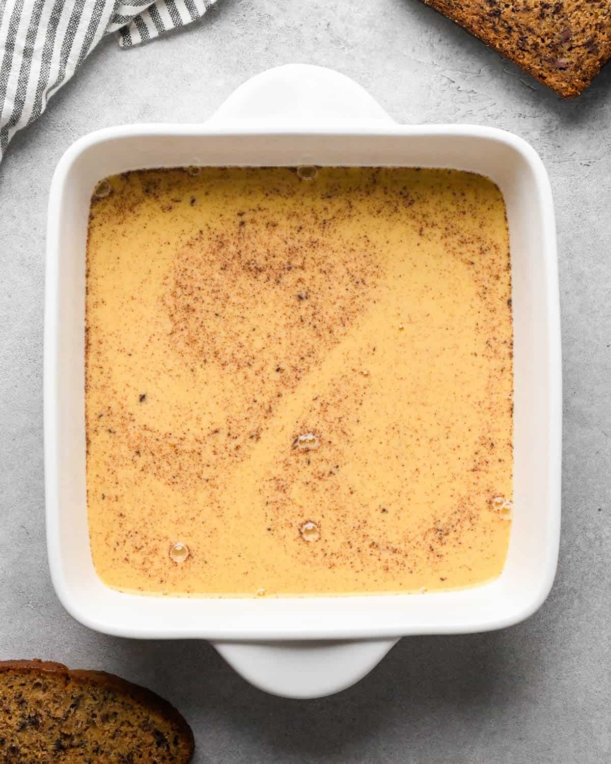 Making banana bread French toast: overhead photo of French toast egg mixture after it has been poured into a white square casserole dish.