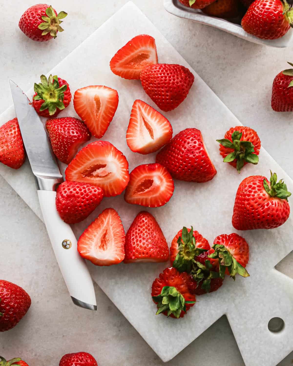 making strawberry cake - hulled and halved strawberries on a cutting board with a knife