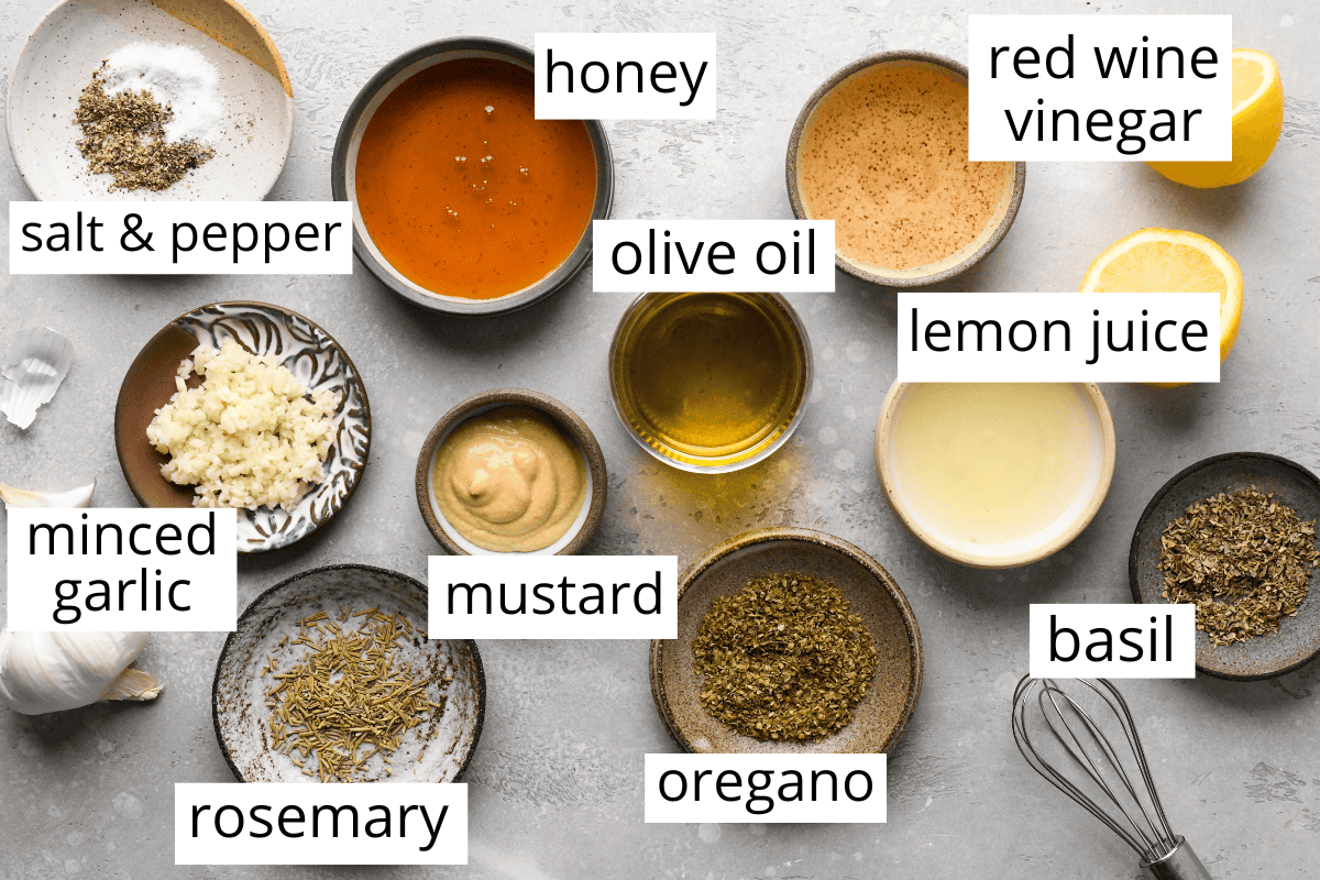 overhead photo of the labeled ingredients in this italian dressing recipe such as honey, olive oil, lemon juice, vinegar, herbs, mustard and garlic