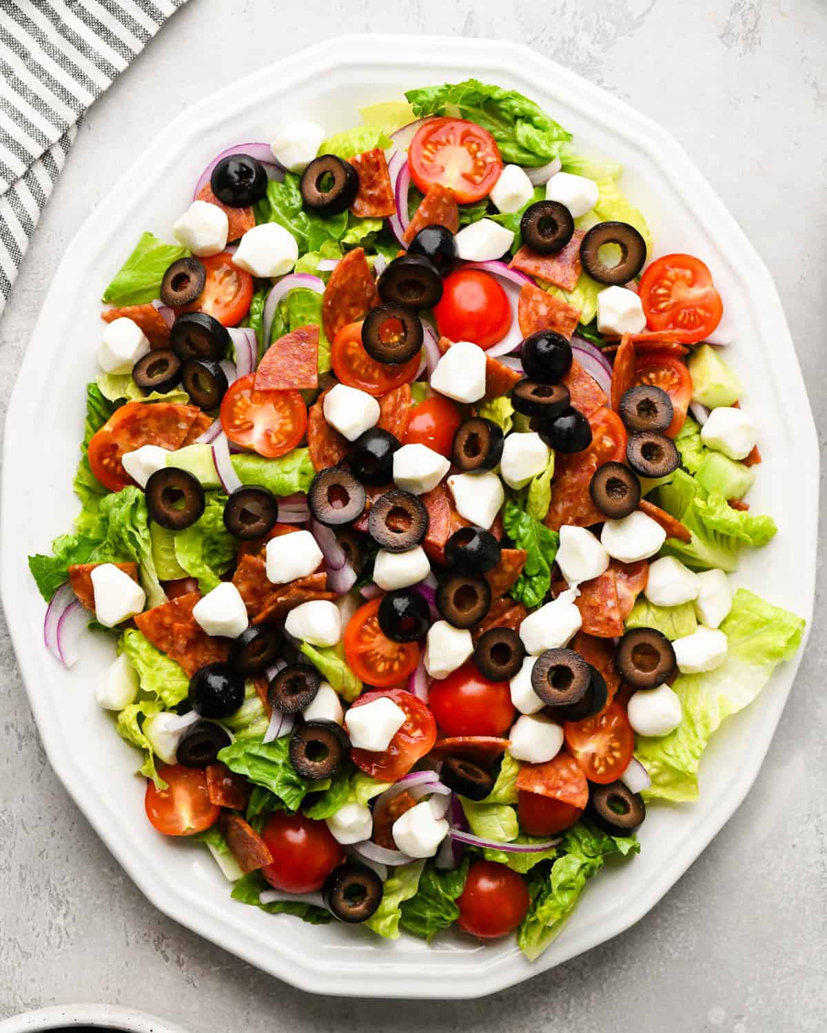 assembling an Italian salad on a white serving plate - added sliced black olives