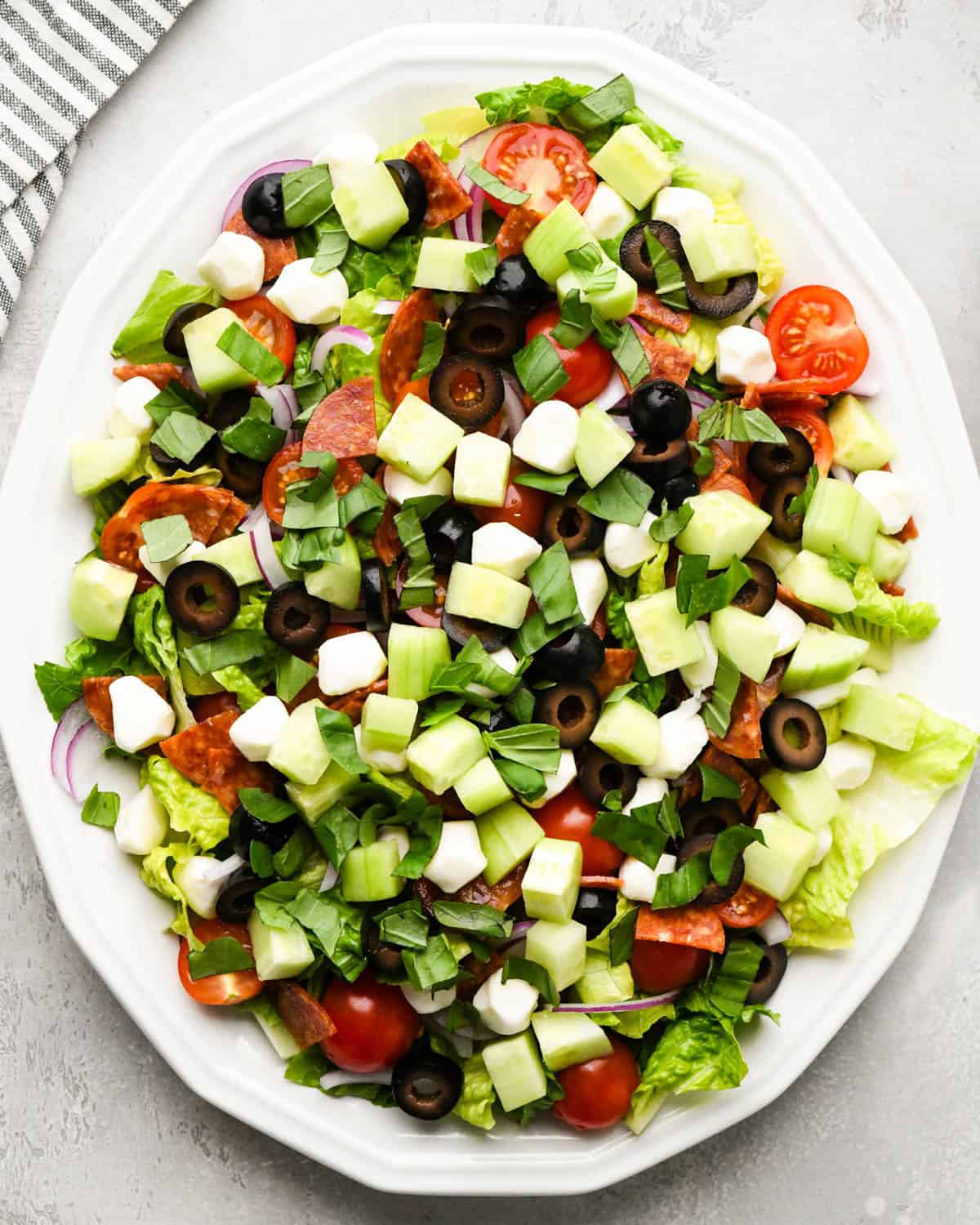 assembling an Italian salad on a white serving plate - added chopped fresh basil