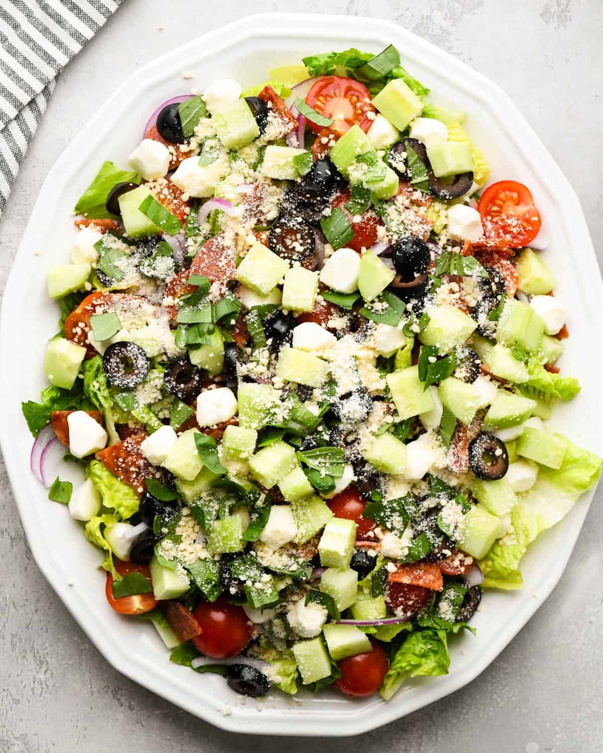 assembling an Italian salad on a white serving plate - added parmesan cheese on top