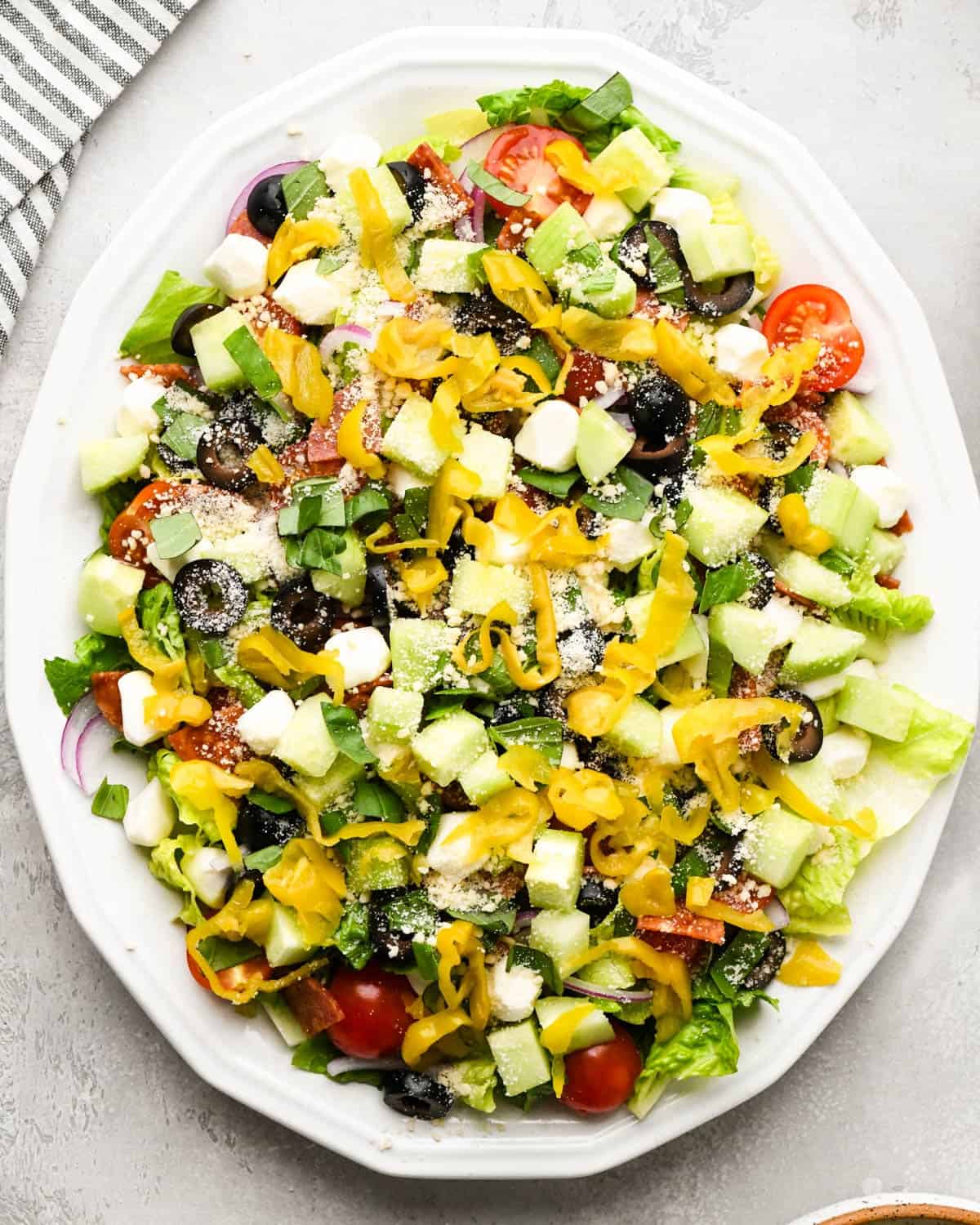 assembling an Italian salad on a white serving plate - added sliced pepperoncinis on top