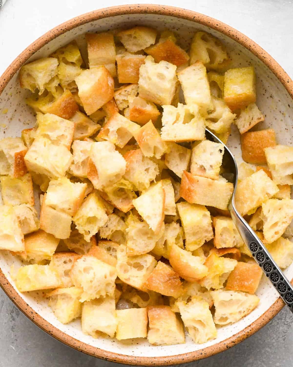 making croutons for Italian salad - bread cubes coated with olive oil in a bowl with a silver spoon