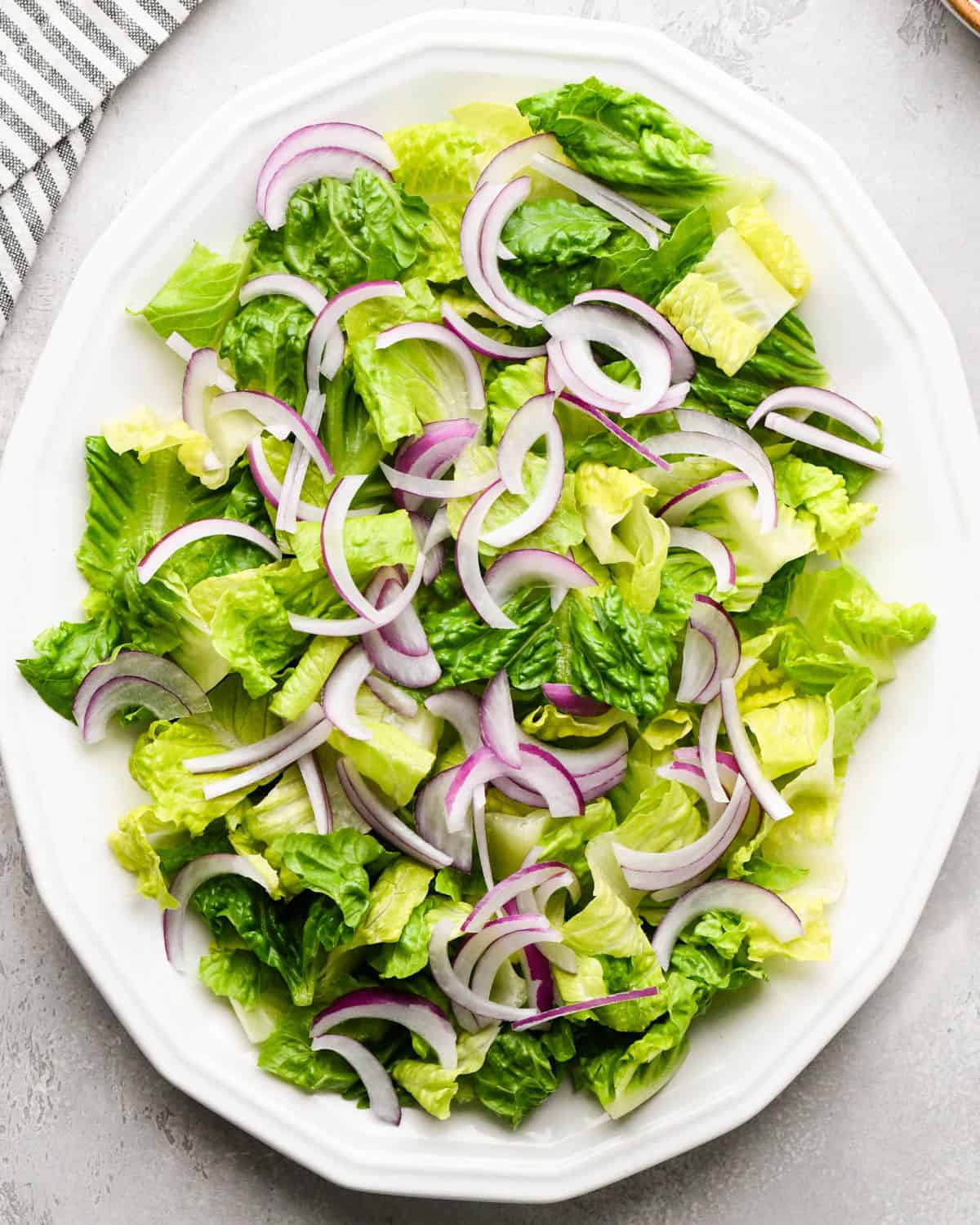assembling an Italian salad on a white serving plate - romaine lettuce and red onions