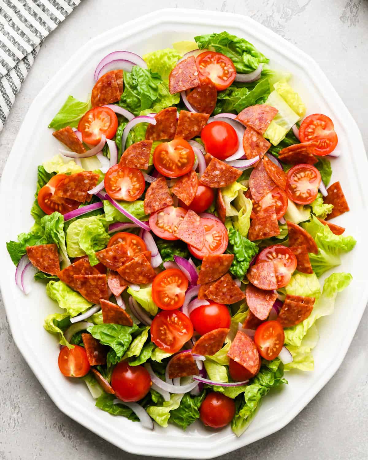 assembling an Italian salad on a white serving plate - added tomatoes and pepperoni