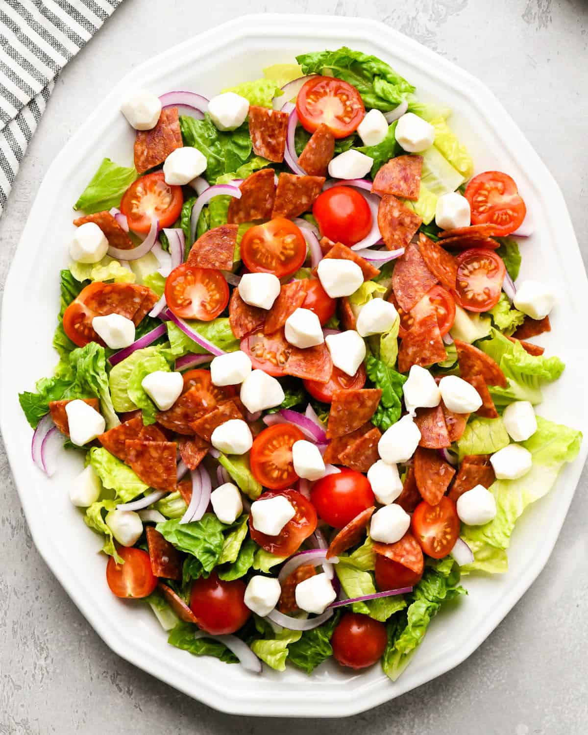 assembling an Italian salad on a white serving plate - added pearl mozzarella