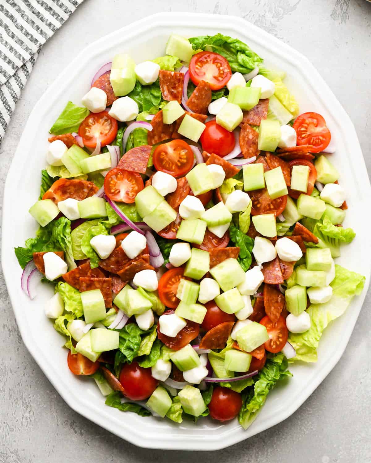 assembling an Italian salad on a white serving plate - added cucumbers