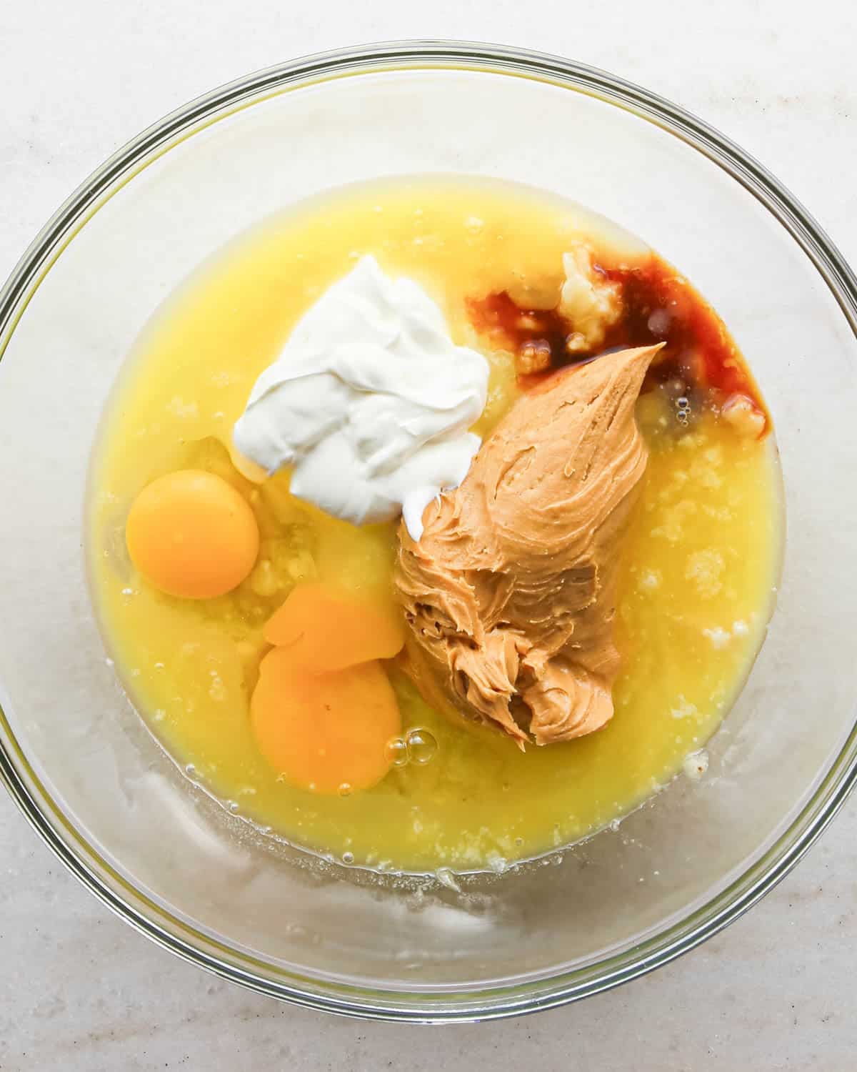 making peanut butter banana muffins - eggs, sour cream, peanut butter and vanilla added to mashed bananas in a glass bowl before mixing