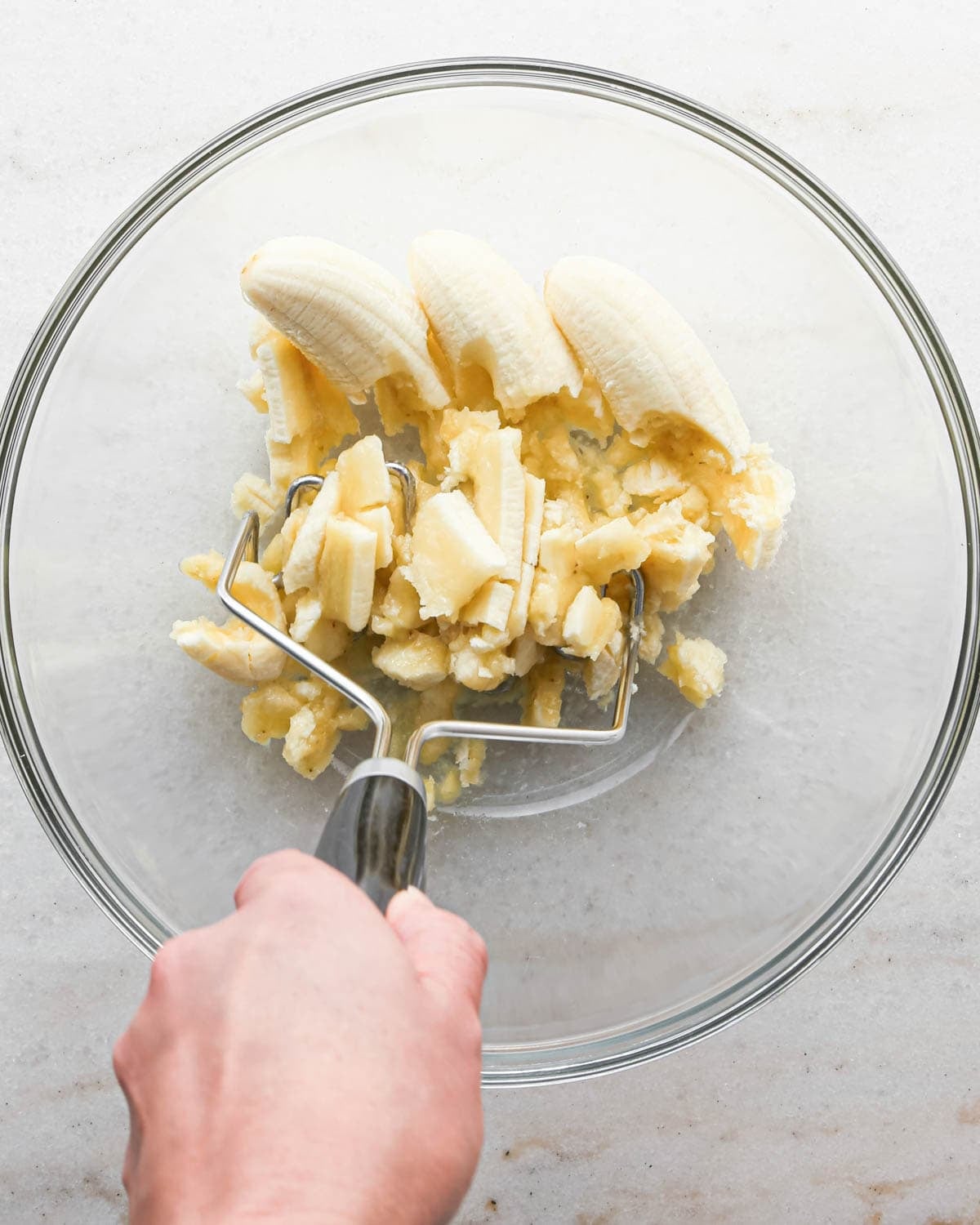 making peanut butter banana muffins - a hand mashing 3 bananas in a glass bowl