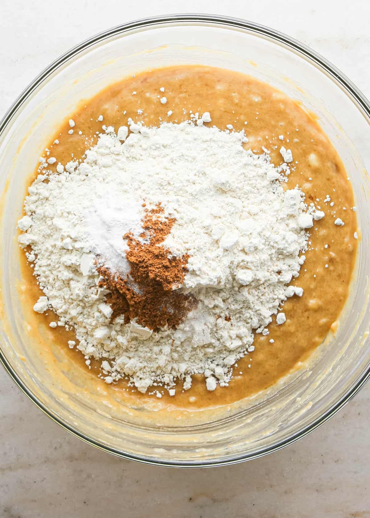 making peanut butter banana muffins - flour, salt, baking soda, baking powder and cinnamon added to the wet ingredients in a glass bowl before mixing