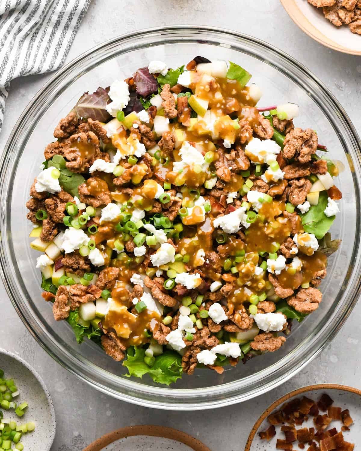 assembling a pear salad - dressing drizzled over the ingredients in a glass bowl