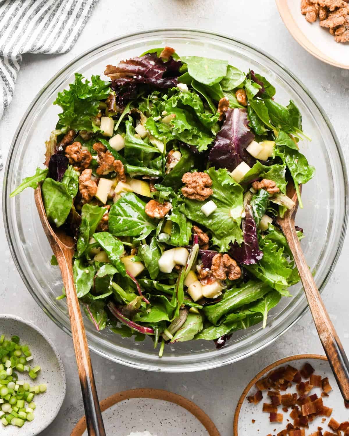 tossed pear salad in a glass bowl with two wooden salad servers