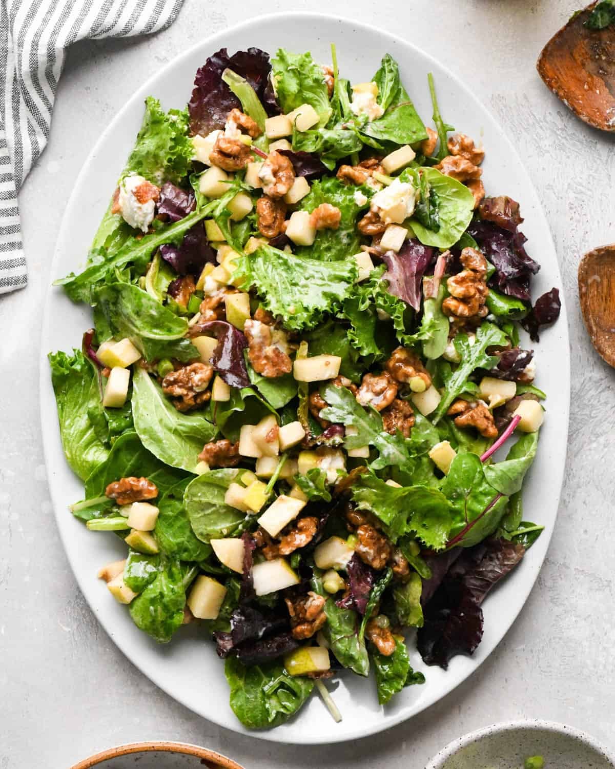 Pear salad with sliced pears, bacon, goat cheese, candied walnuts, green onions, and mixed greens, tossed in a homemade balsamic vinaigrette on a white serving platter.