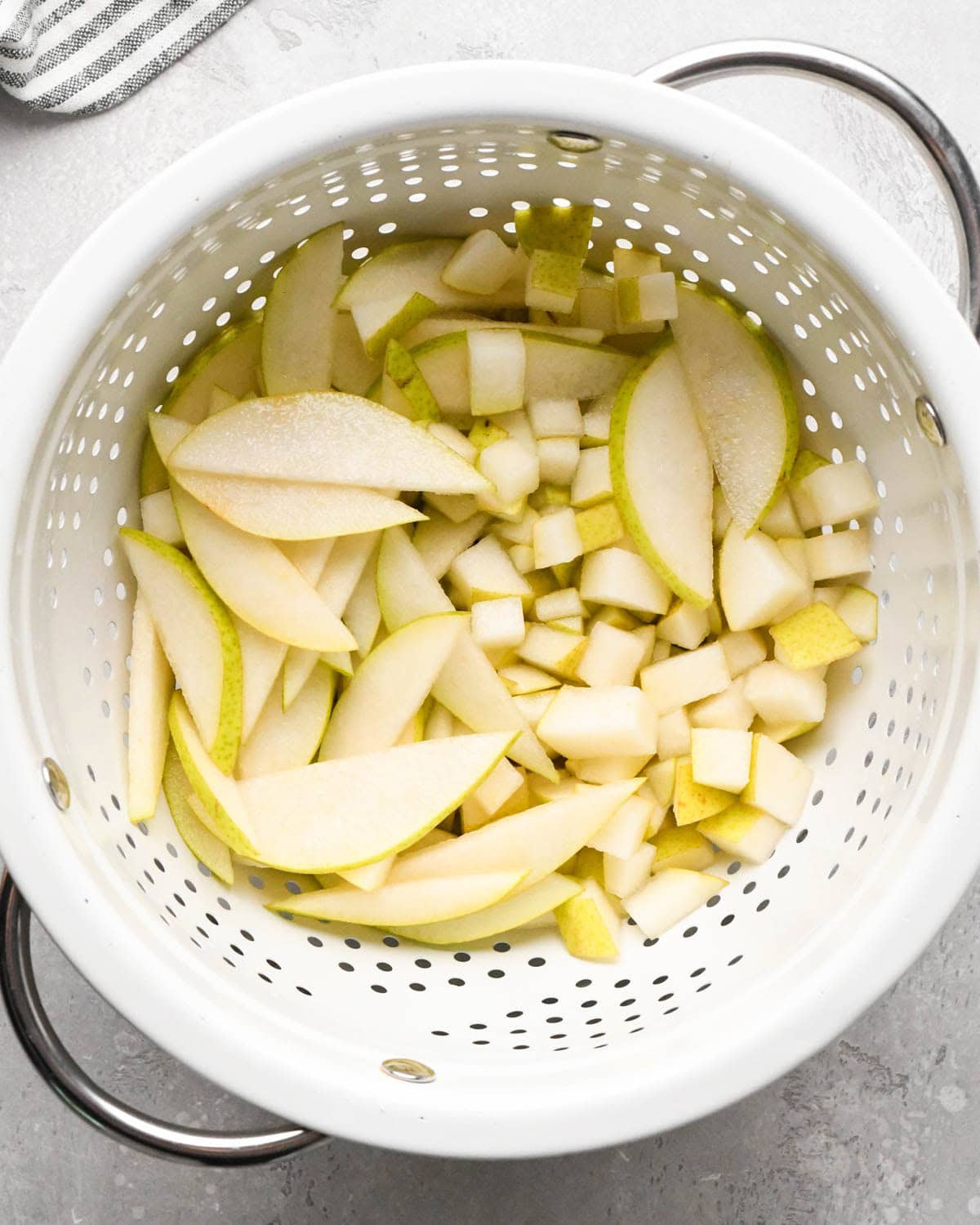 how to make pear salad - diced and sliced pears being drained in a white colander with silver handles